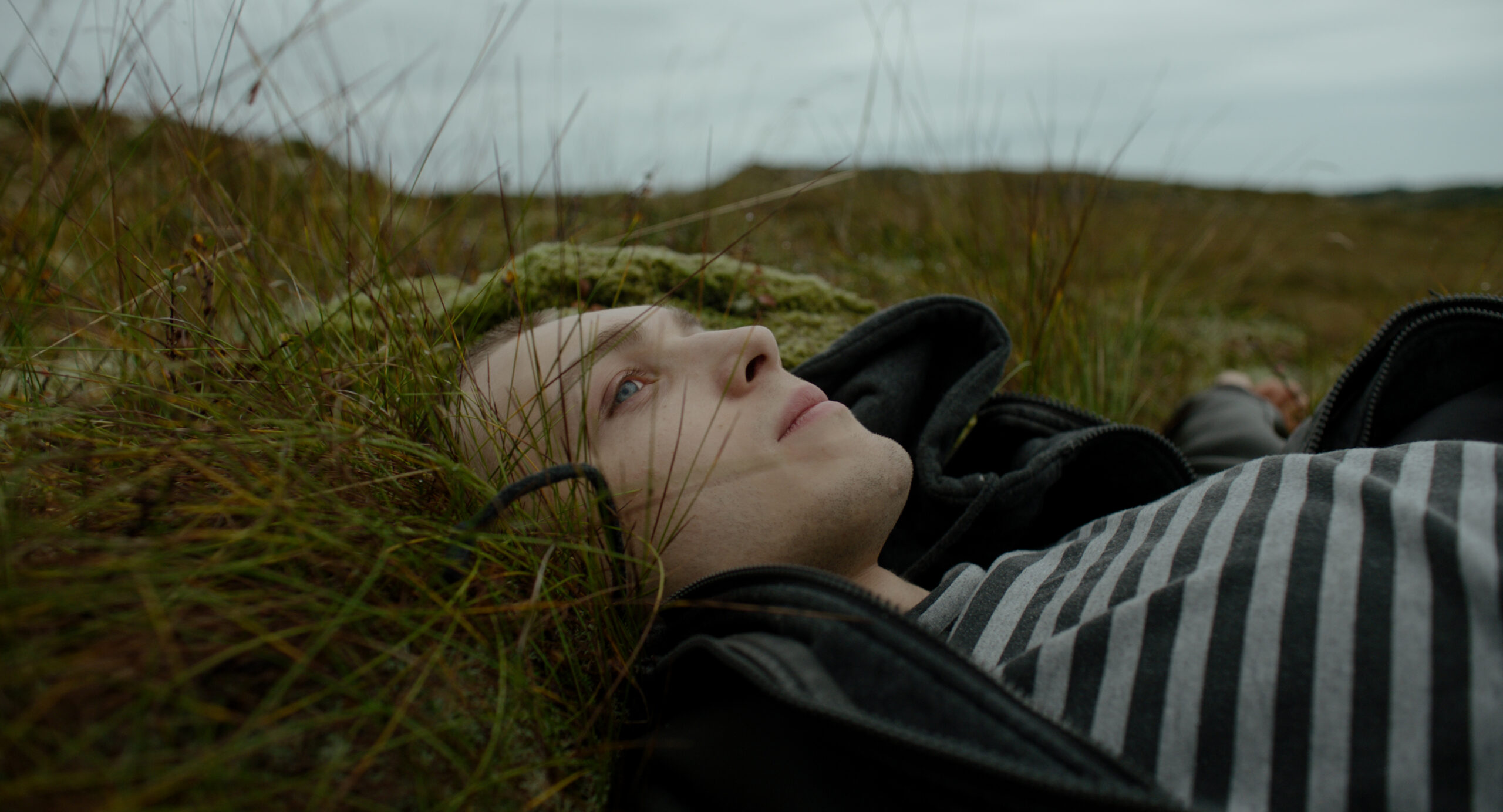 En person ligger i gresset og ser på himmelen. Bilde fra filmen.