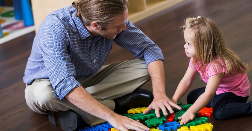 En liten jente sitter på gulvet og leker med puslespillbiter sammen med en voksen mann