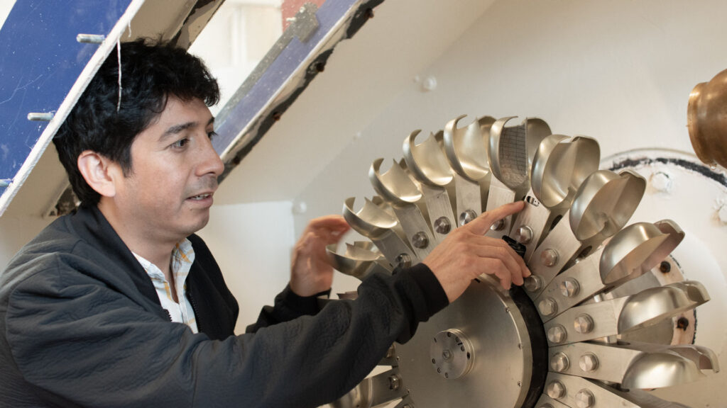 researcher points at metal turbine. photo