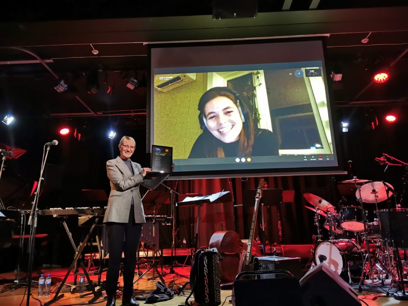 Rektor Borg holder opp diplomen, prisvinner Anja Lauvdal er digitalt til stede via skjerm i bakgrunnen.
