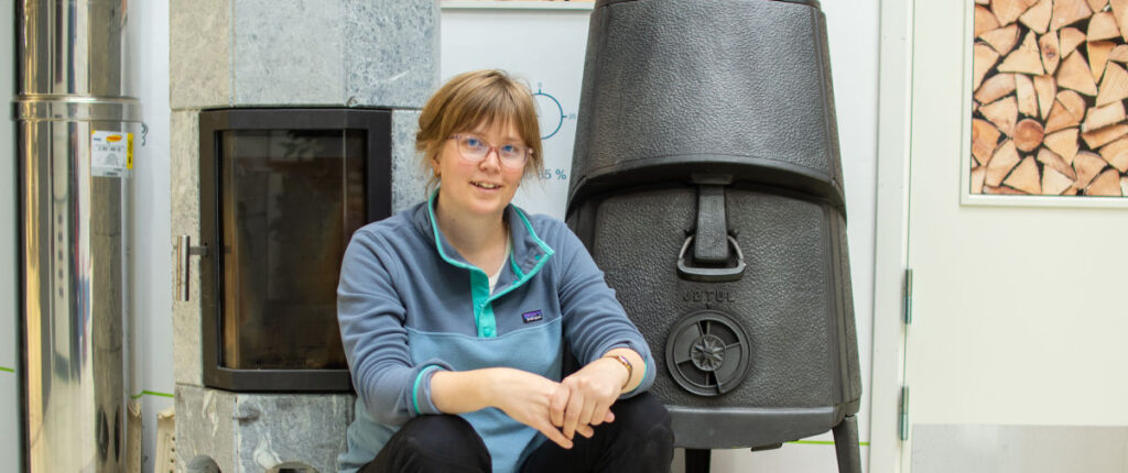 A photo of a woman in front of a woodstove.