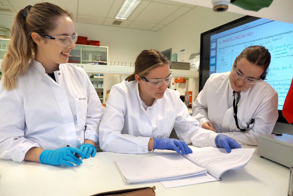 Et bilde av 3 kinnelige studenter på lab som ser på noen papirer.