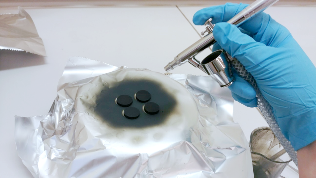 Et bilde av produksjon av membraner, som viser fire sorte rundinger som sprayes med noe svart.