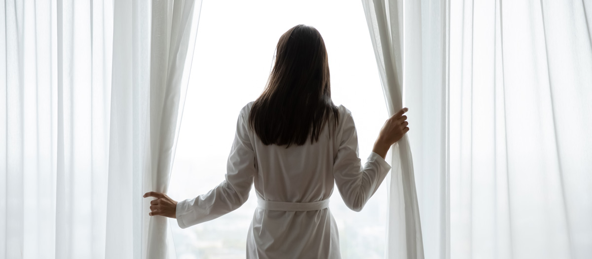A woman standing in the window with curtains.