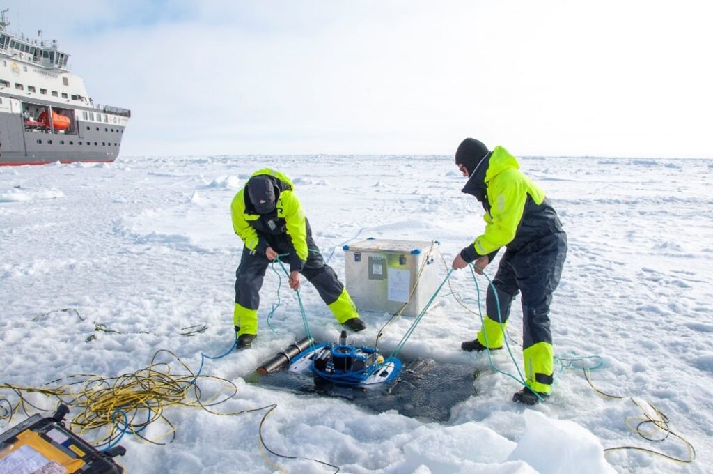 Two people working on the ice, launching a mini ROV.