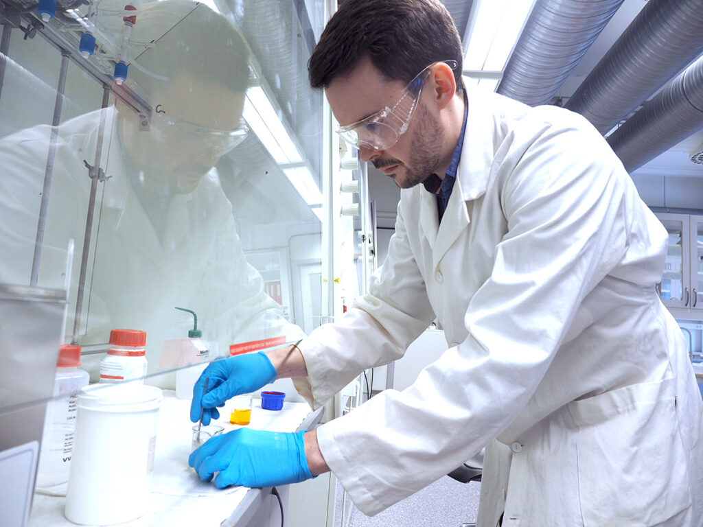 En mann i labfrakk som jobber med kjemikalier på et laboratorium.