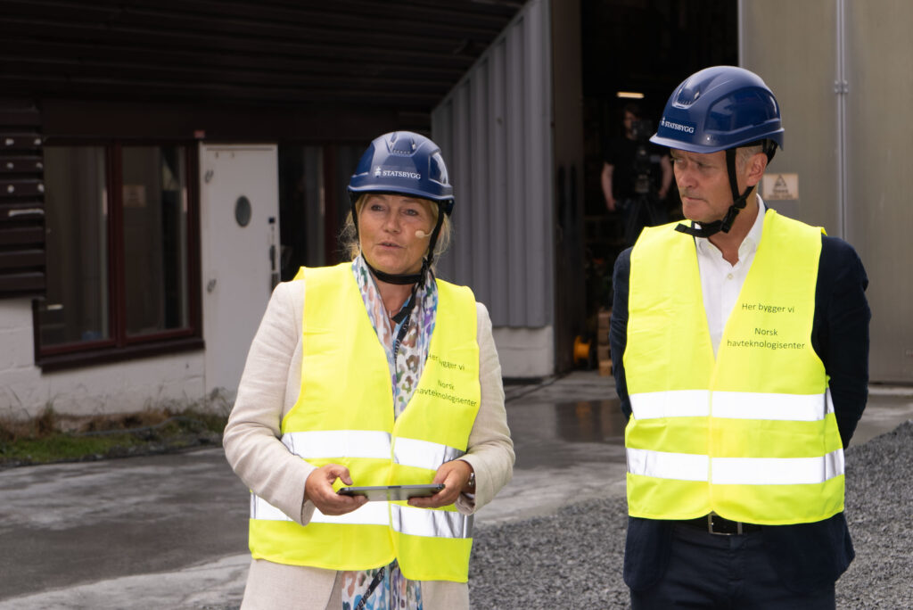 Alexandra Bech Gjørv, konsernsjef i Sintef holder tale, med byggherredirektør i Statsbygg Marius Tunstad ved sin side. Begge har på hjelmer og gule vester. Bildet er tatt på en byggeplass 