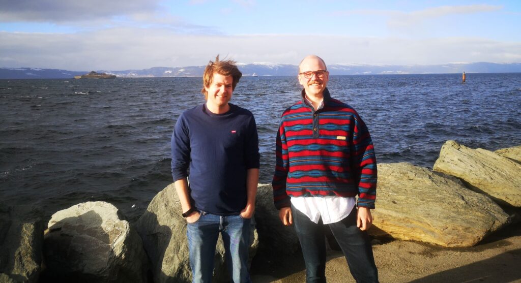 A photo of two men in front of the ocean.