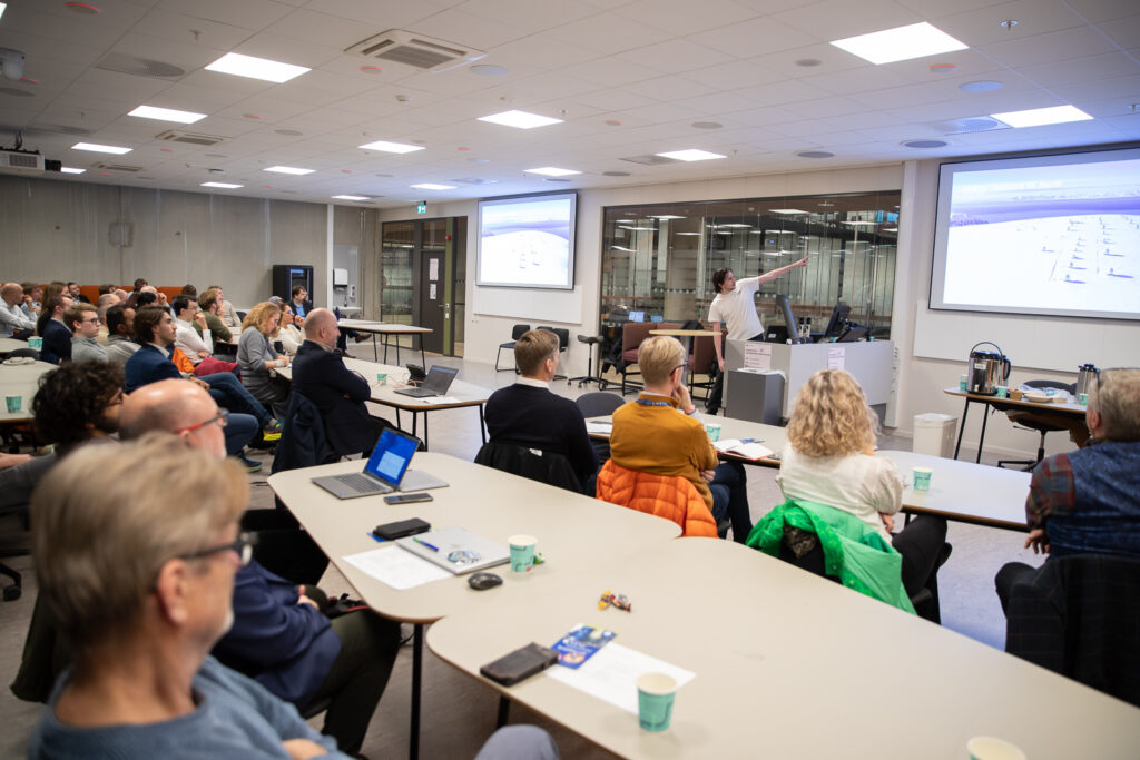 Philip Kværneng, tidligere student ved NTNU, nå med jobb i KSAT, Kongsberg Satellite Service peker på skjermen med diverse publikum i salen.